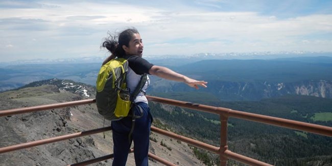 A young woman looks across a mountain range on a windy day