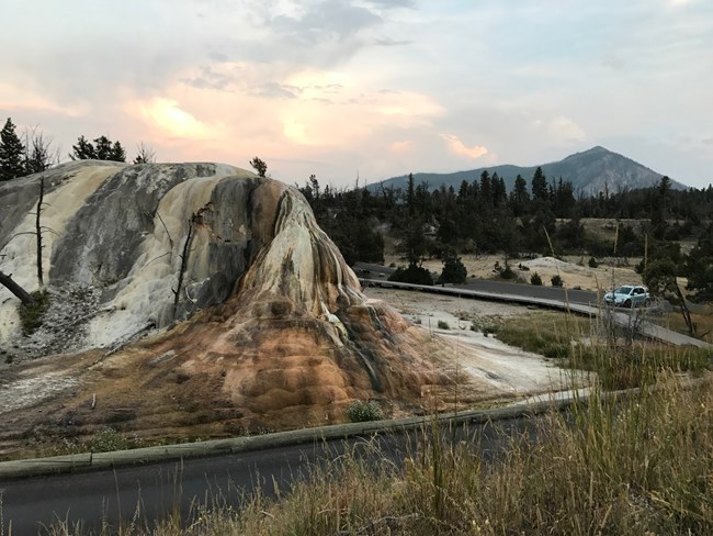 A hill-shaped hydrothermal feature cascades water down the orange flanks of the feature.