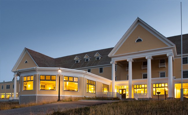 A large lodge with yellow paint and white columns in the evening light