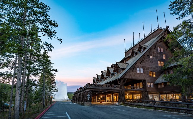 A large, rustic lodge in front of an erupting Old Faithful geyser