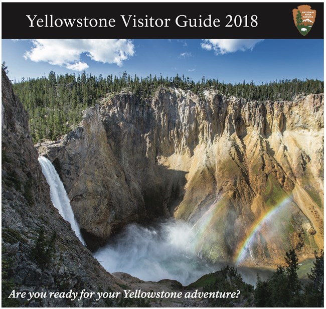 Yellowstone Visitor Guide 2018 cover Top part of the newspaper cover, with the title and NPS arrowhead in a black bar, and a panoramic view of the Lower Falls and a rainbow below
