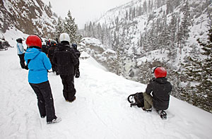 A group of visitors stands in front of the snow-covered scenery of Firehole Falls. A group of visitors stands in front of the snow-covered scenery of Firehole Falls.