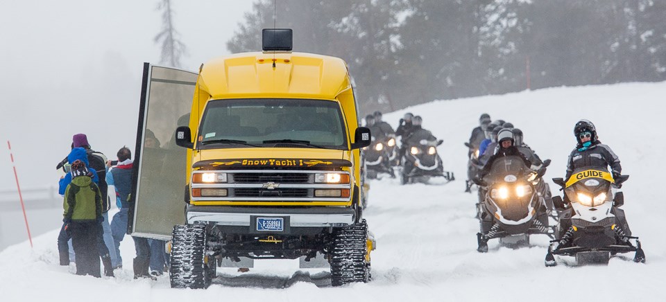 Snowmobiles pass by a snowcoach pulled over to let visitors view Midway Geyser Basin