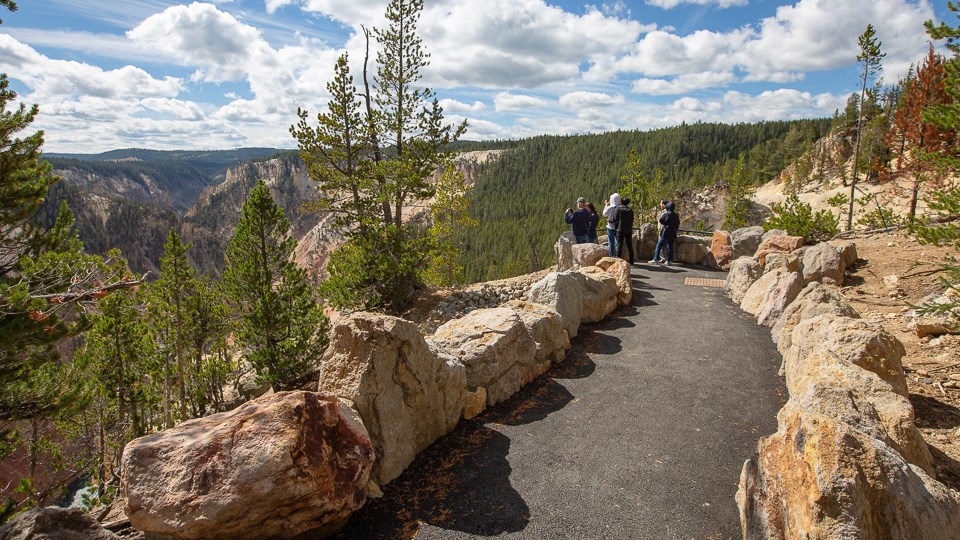 A paved walkway leads to an overlooks where people are looking into a canyon