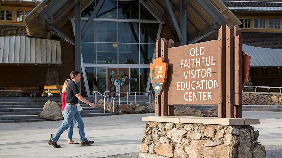 Couple walks in front of Old Faithful Visitor Education Center.