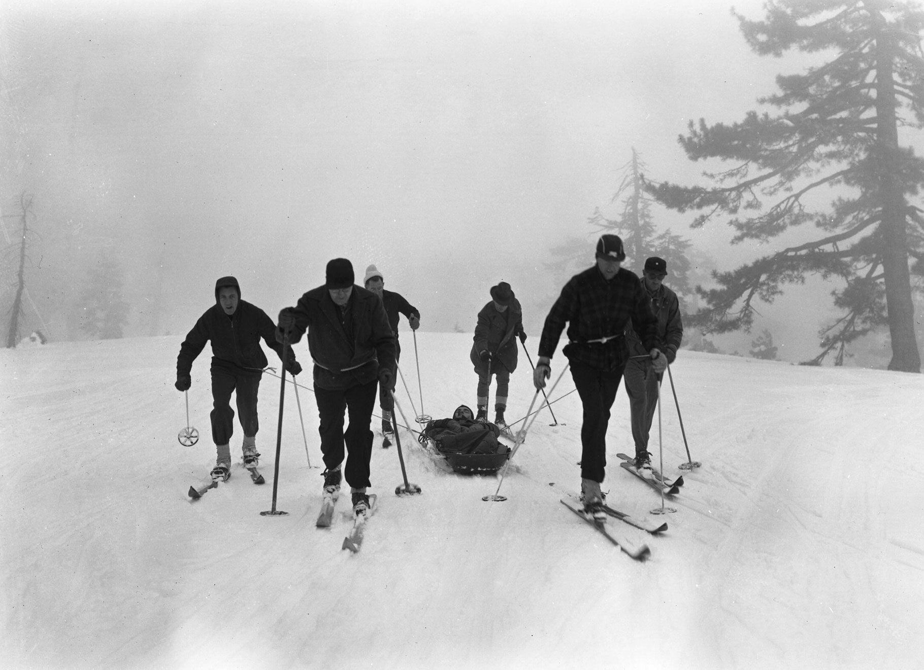 Black and white photo of skiers pulling a sled with a patient in it