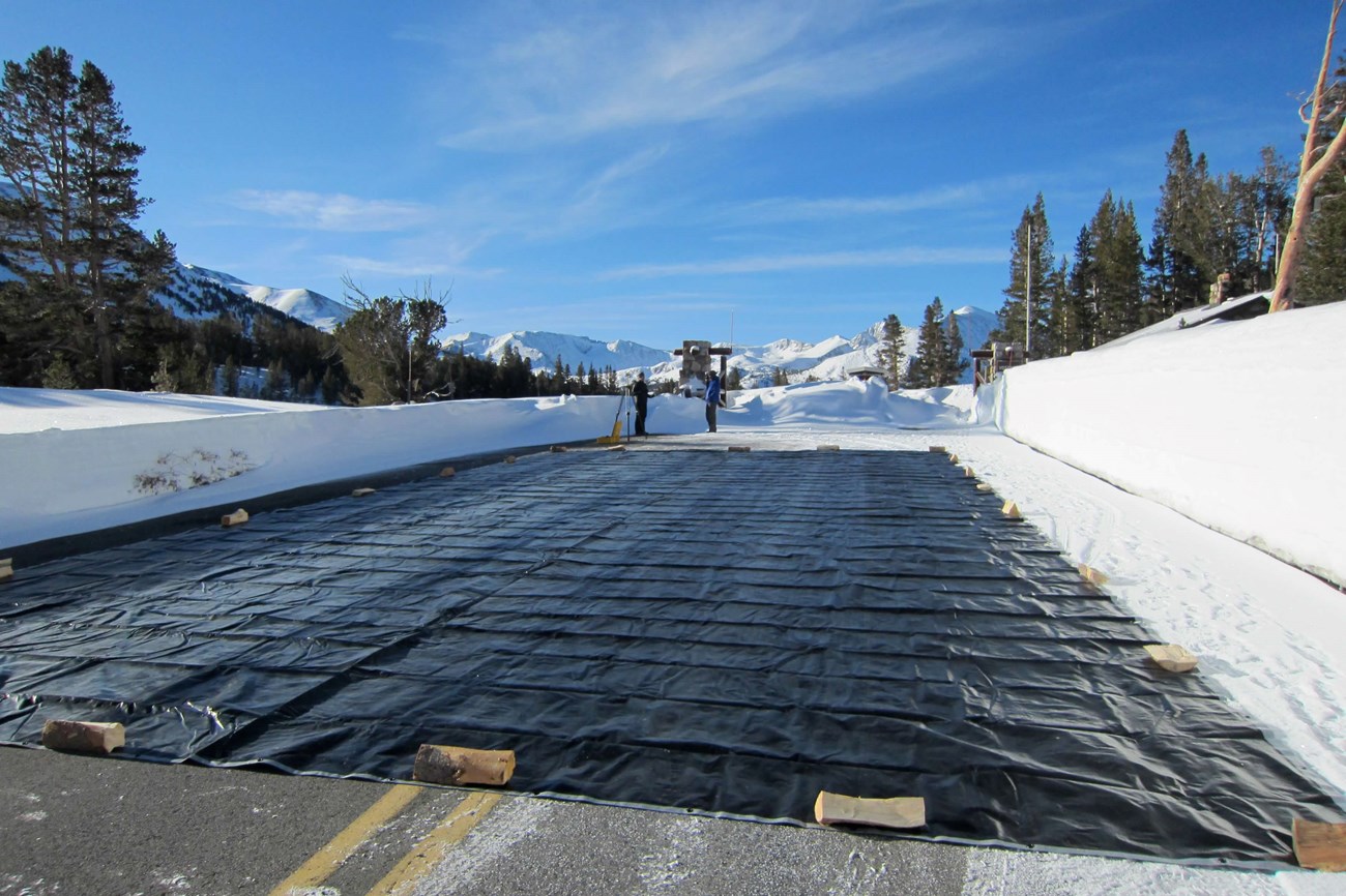 Large black tarp laid upon plowed road surrounded by snow at Tioga Pass