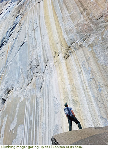 Ranger looking up at a striped and water stained granite wall.