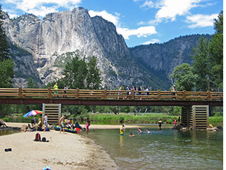 People along the calm Merced River at Swinging Bridge