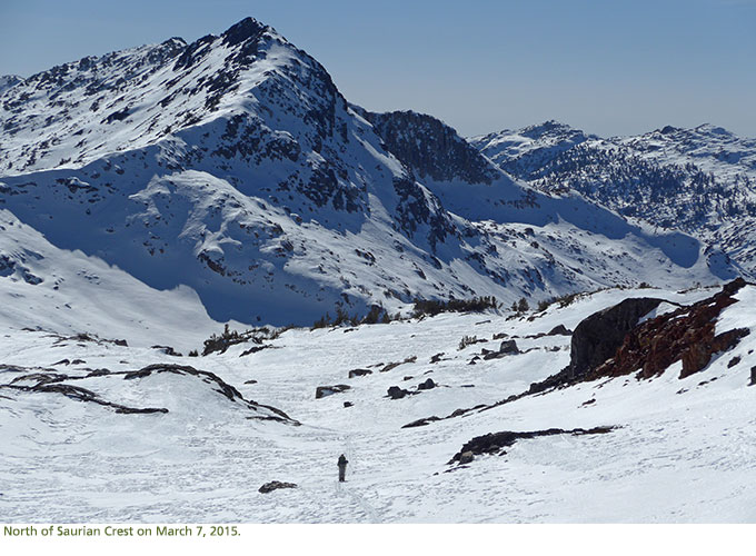 A skier skiing away towards snow covered mountains.