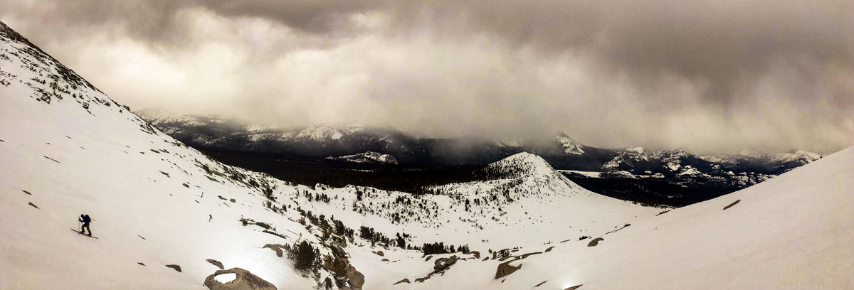 Skier ascending mountain under cloudy skies