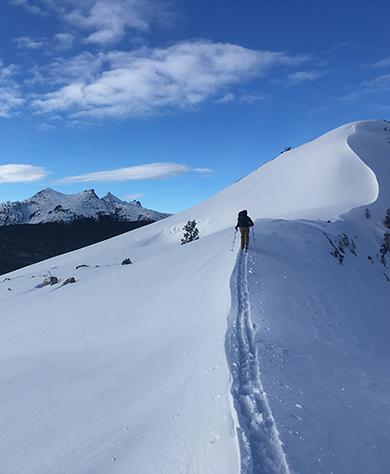 Cross-country skier on steep snowy slope under blue skies.