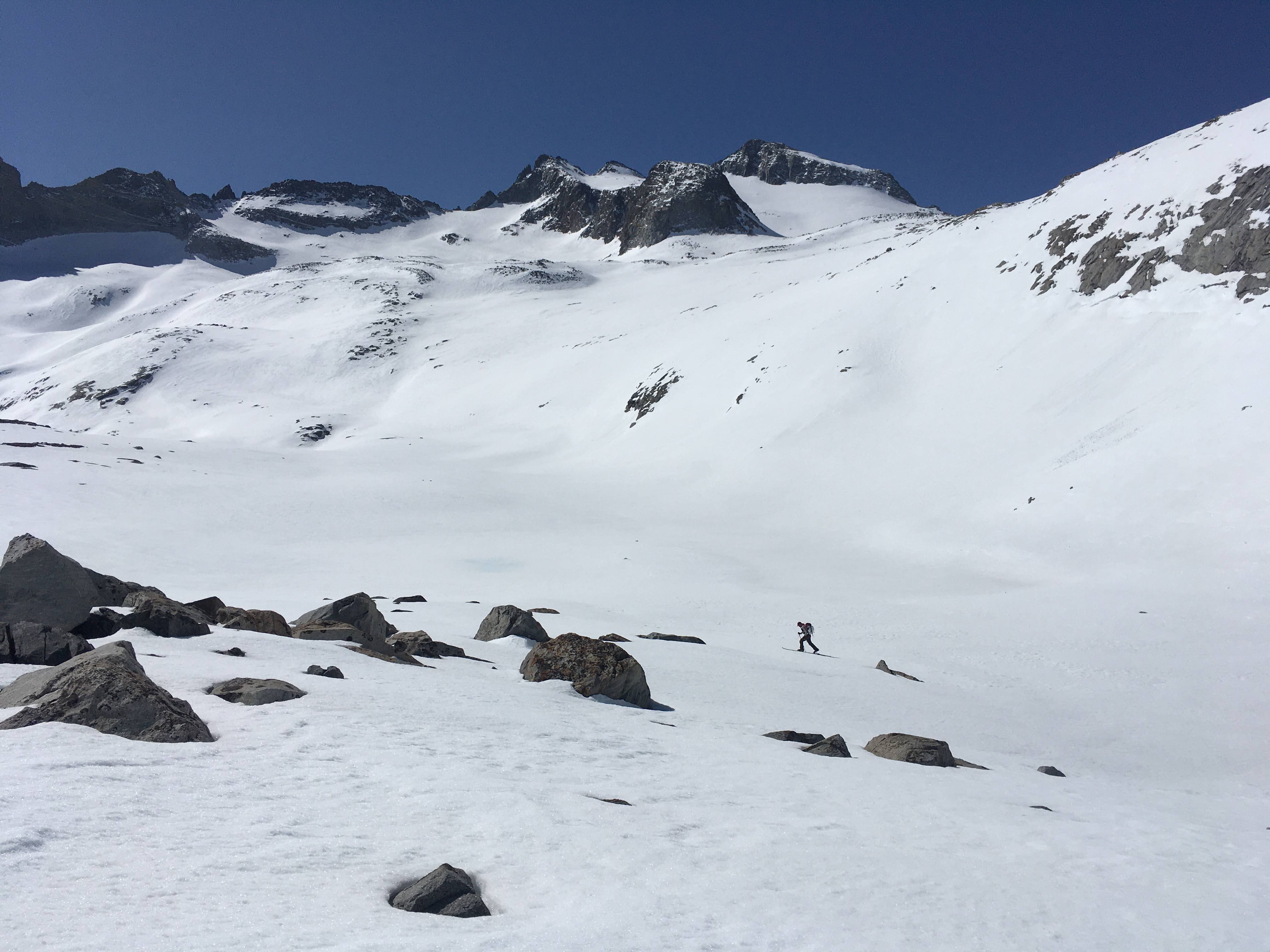 Snowy mountain landscape with skier skiing uphill in the distance.