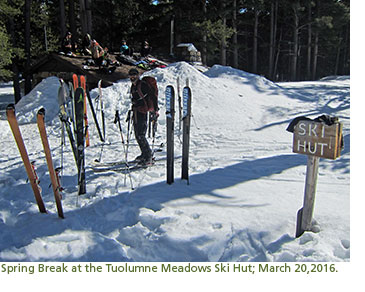 Backcountry skiers relaxing outside of a cabin, surrounded by snow.