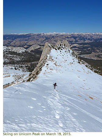 A skier on a snowy Unicorn Peak with mountains in the distance.