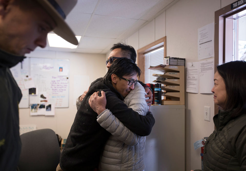 Two people hug while another person and a ranger stand by