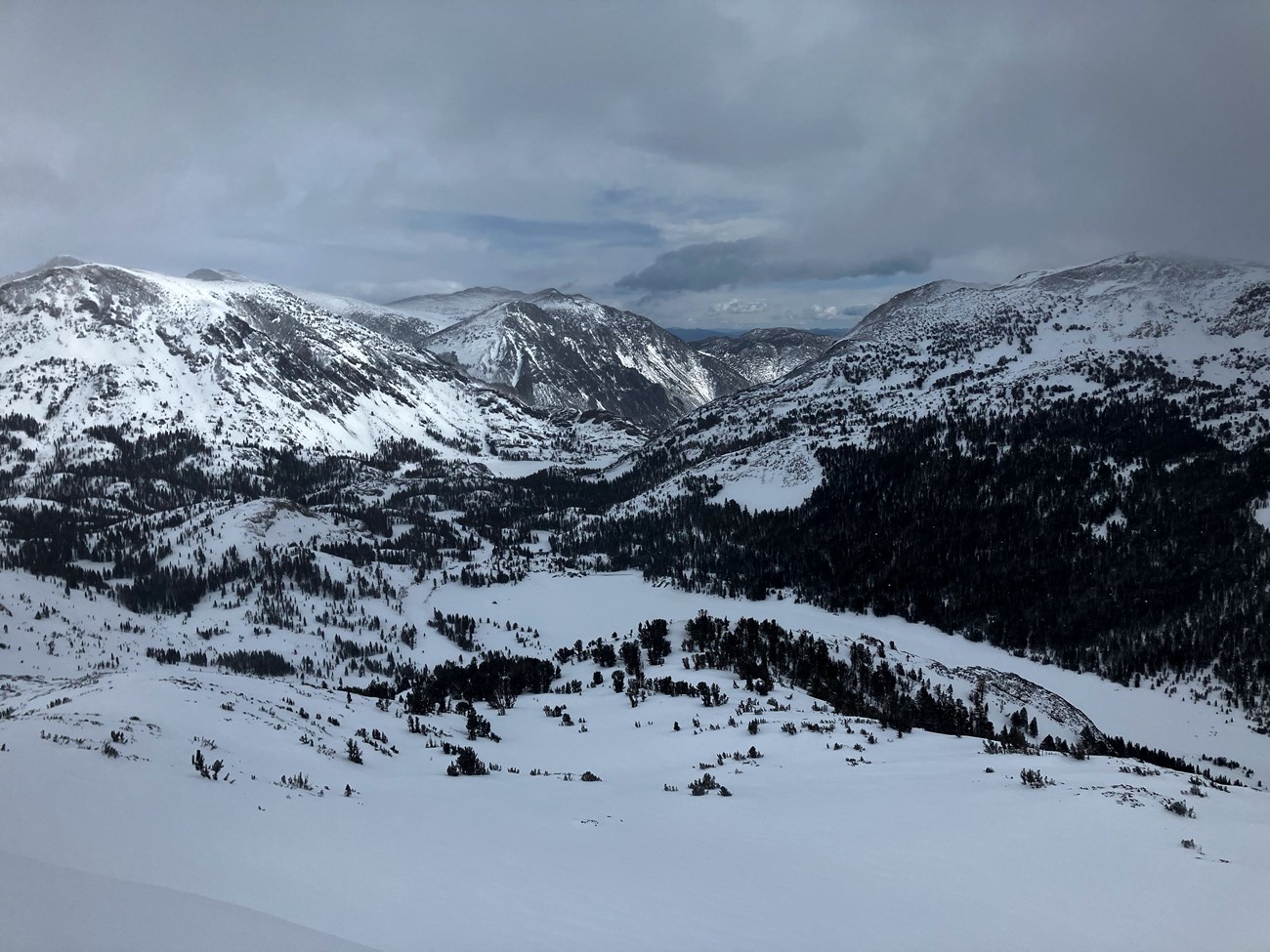 View from above looking down a snowy canyon with a few snow-covered lakes on a cloudy day