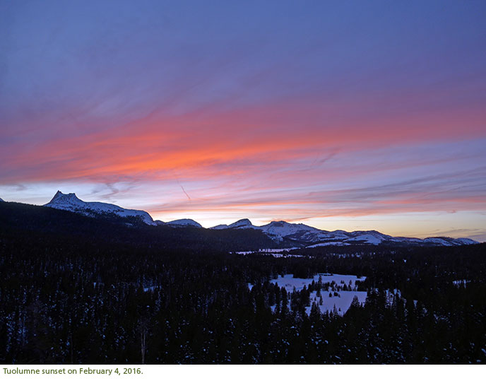 Pink sunset clouds hover over a snow covered landscape.