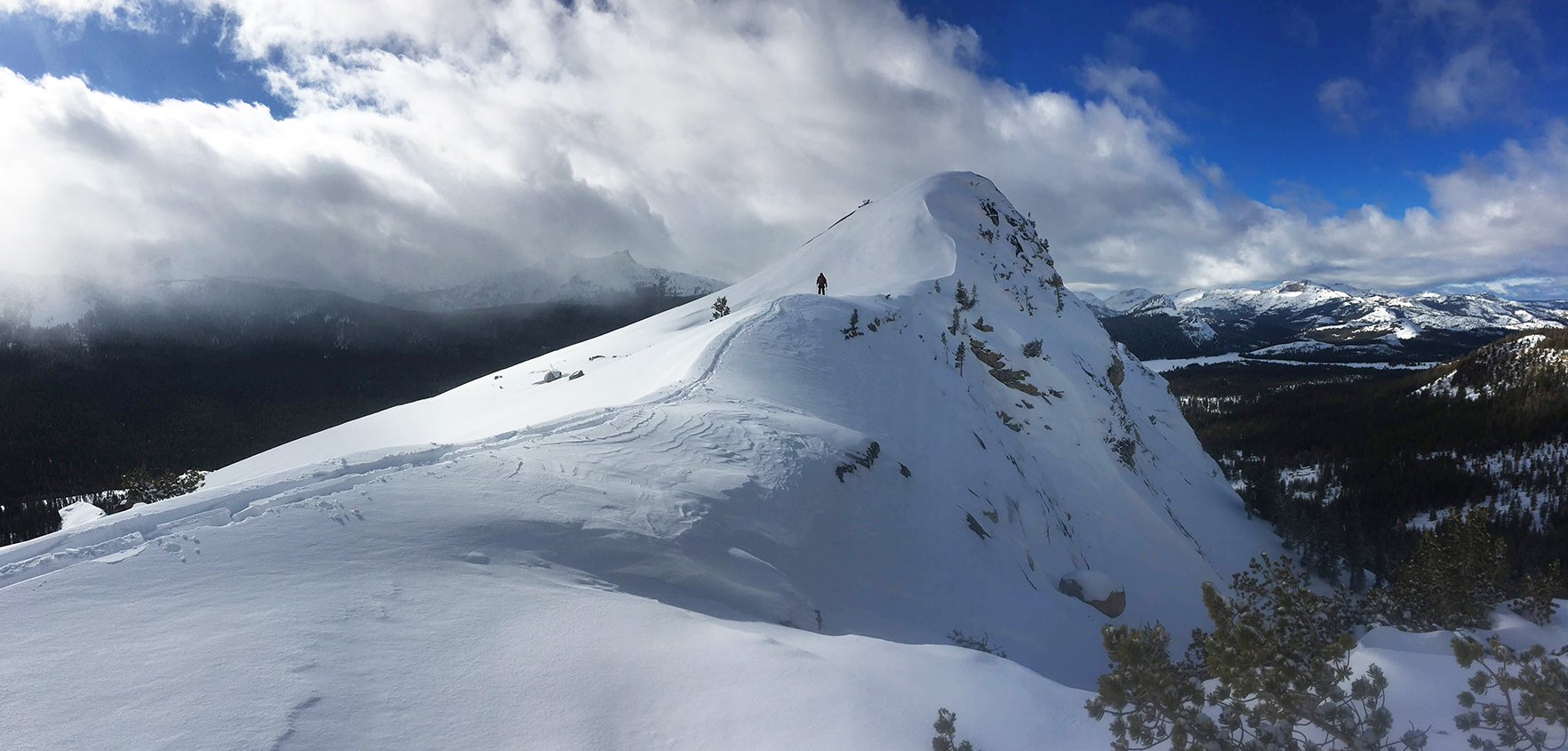 Cross-country skier on side of snowy slope, with snow-capped peaks in background.