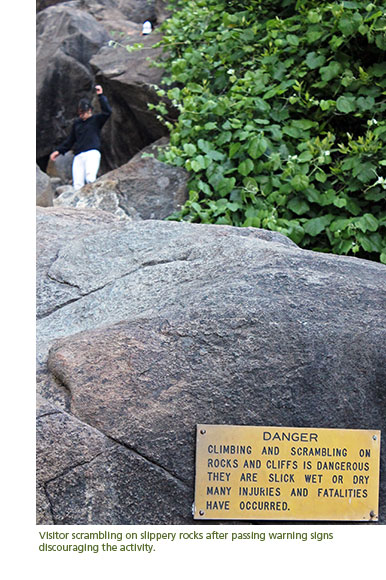 Visitor scrambling on slippery rocks after passing warning signs discouraging the activity.