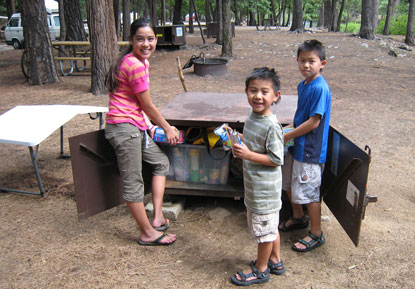 3 children stand next to an open bear box filled properly with their human food