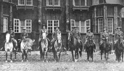 Eight mounted rangers pose in front of big windows on the Rangers' Club where they lived