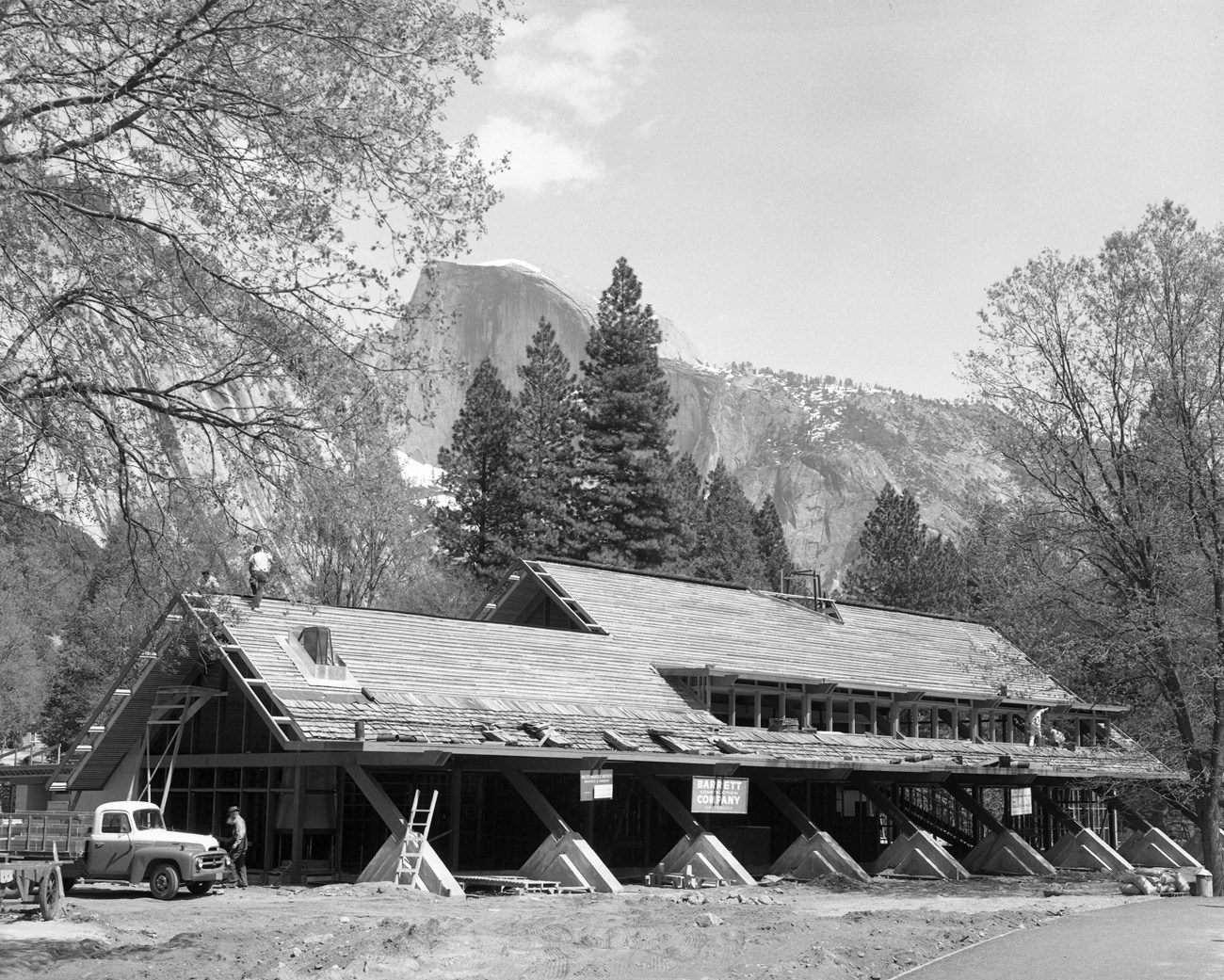 A-frame building under construction; ladders and a work truck are nearby, Half Dome is in the background