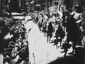 Dozens of uniformed soldiers stand on a fallen sequoia tree