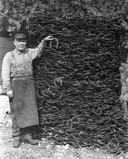 Government blacksmith Fred Bruschi with stack of horseshoes, 1927