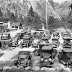 Multiple cars parked with cliffs in background.