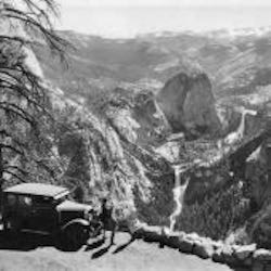 Automobile parked with waterfalls and canyon in background.