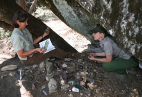 Archeologists sit under rock to sort artifacts at a site