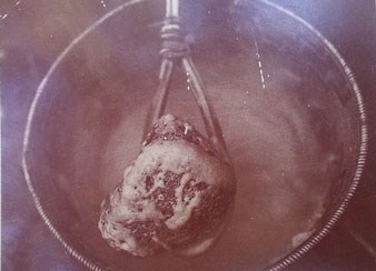 Hot cooking stone being removed from basket of cooked acorn mush.