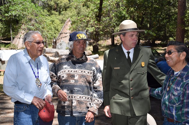 Four people in formal clothing walking together in front of umachas in Wahhoga Village.