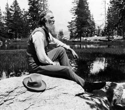 John Muir sits on rock with lake behind