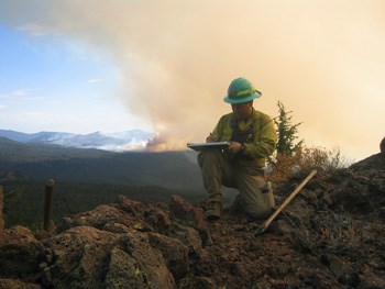 A firefighter takes notes with smoke behind him