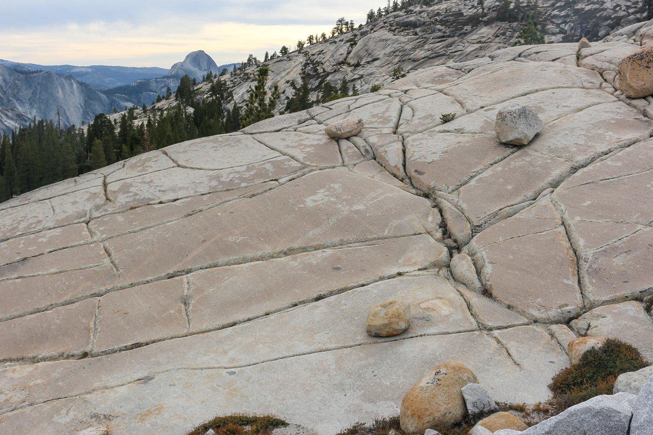 Granite with many perpendicular fractures, with boulders scattered on top. Half Dome is visible in the distant background.