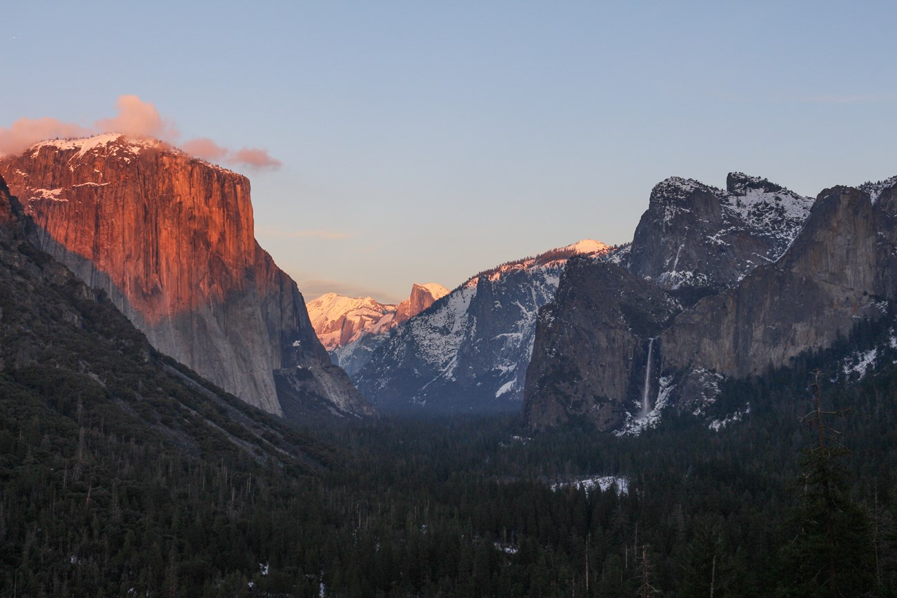 Photo from Tunnel View showing Yosemite Valley with sheer cliffs surrounding a flat valley floor.
