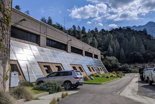 Large black solar panels gleam in the sun on a slanted concrete building wall.