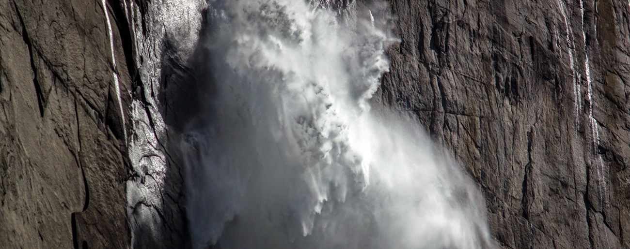 White spray rushes against a background of granite cliff.