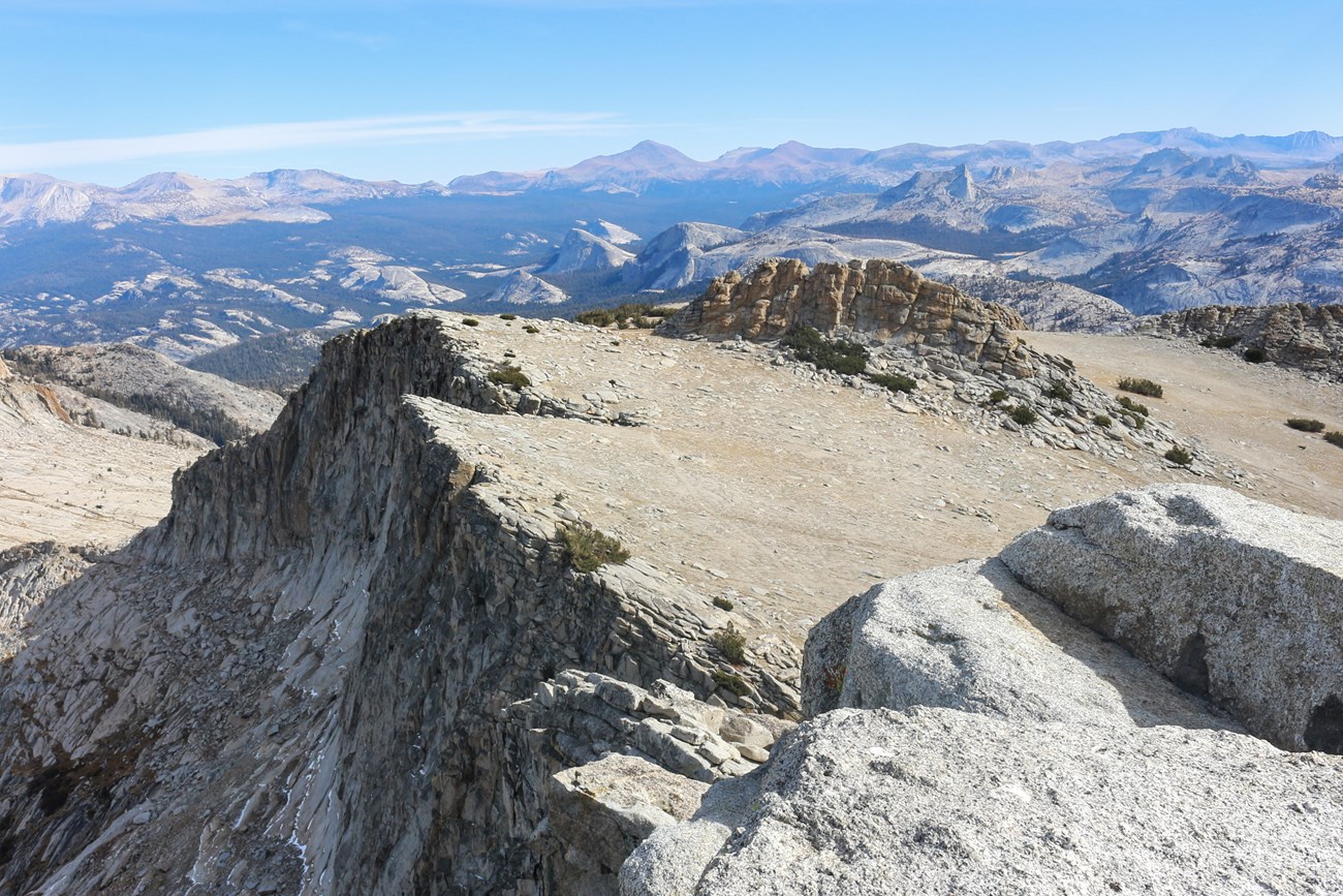 Slanted mountaintop leading to a cliff with mountain peaks in the background