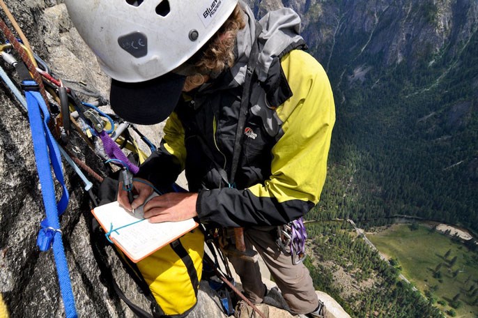 Rock climber on the side of El Capitan making notes in a notebook
