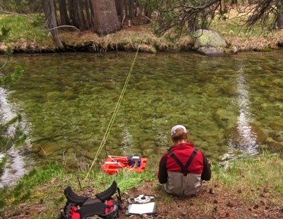 Person sits on stream bank with stream measurement equipment