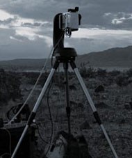 Camera on tall tripod is placed in open meadow to snap landscape images