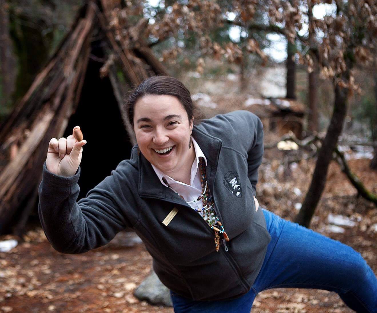 Woman in an excited pose holding an acorn; bark house in the background