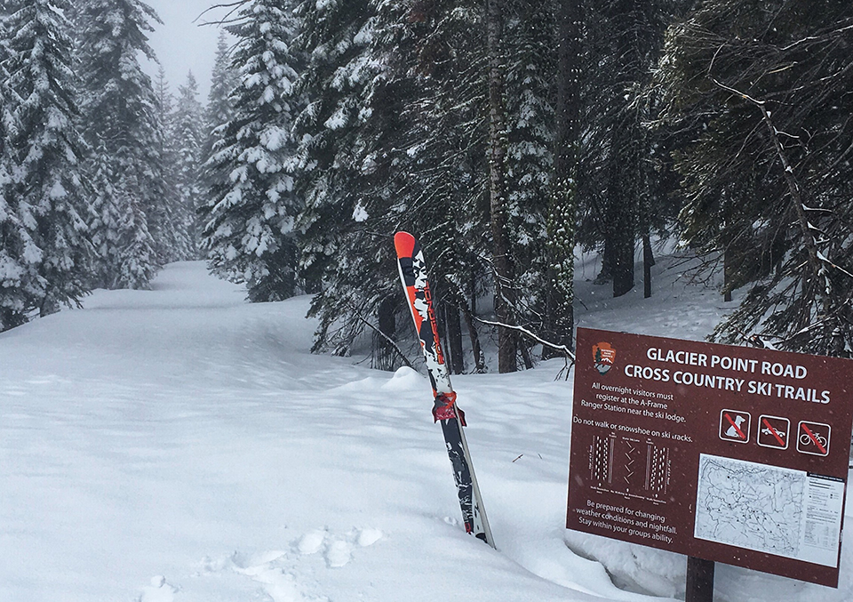 Glacier Point Road Cross Country Ski Sign with snow covered road and a pair of skis Glacier Point Road Cross Country Ski Sign with snow covered road and a pair of skis