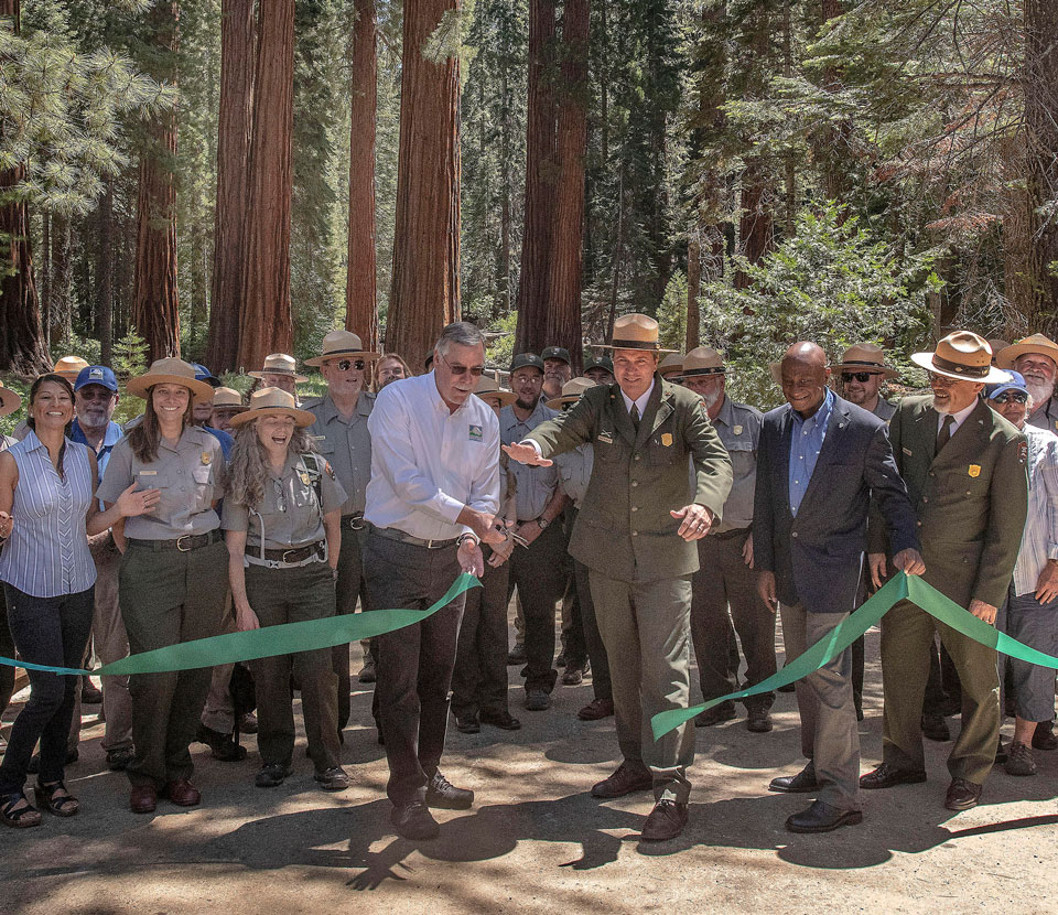Mariposa Grove ribbon cutting Rangers and other employees standing behind ribbon at superintendent and YC president cut the ribbon