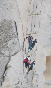 Two men hang onto cables ascending rockface