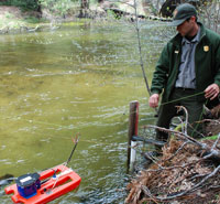 Ranger stands on side of river with monitoring equipment in the water
