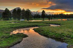Sunset over a grassy meadow with a river running through it.